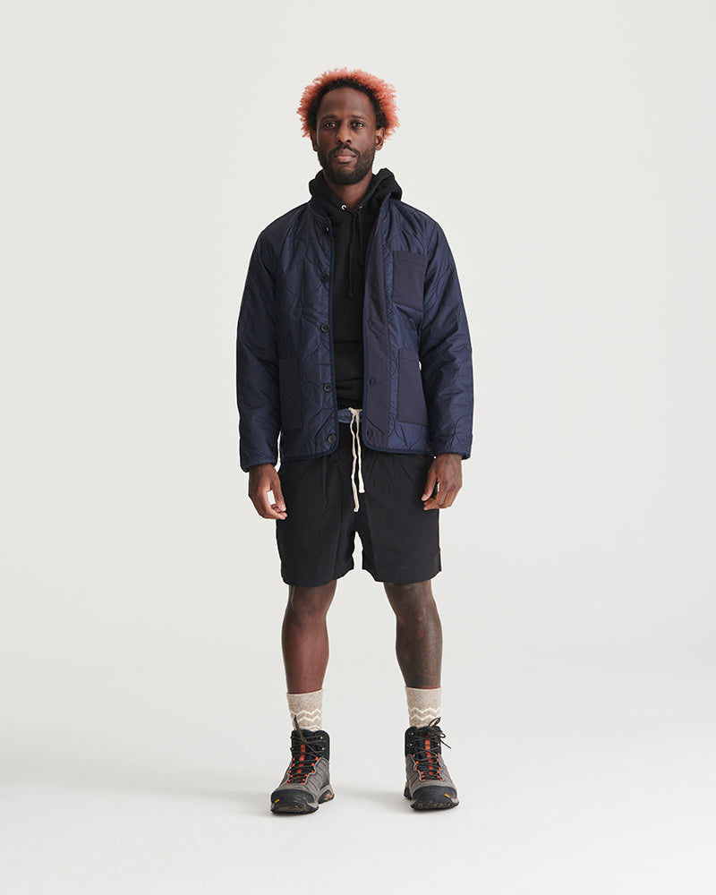 Night Sky Bison Ultralight Liner Jacket (In-use): Man wearing open navy quilted jacket over black hoodie and shorts
