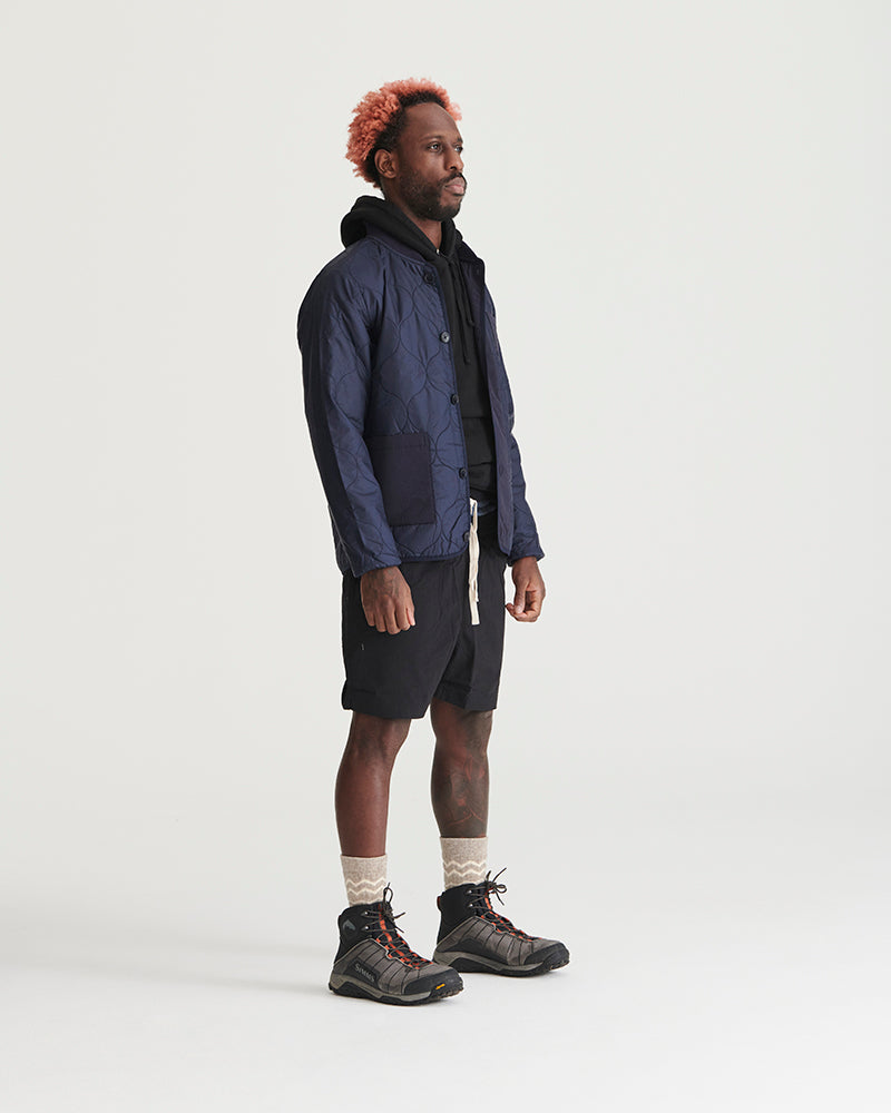 Night Sky Bison Ultralight Liner Jacket (Angle): Man wearing navy quilted button-front liner jacket with black shorts and hiking boots