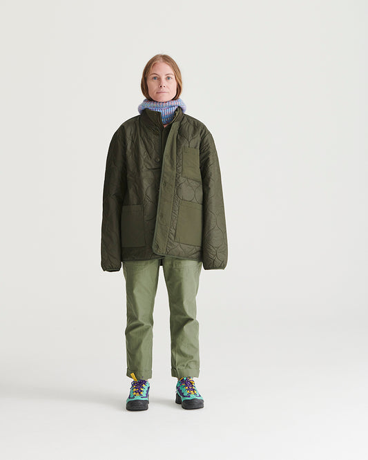Forest Floor Bison Ultralight Liner Jacket (In-use): Woman wearing olive quilted liner jacket, open front, green trousers, colorful sneakers