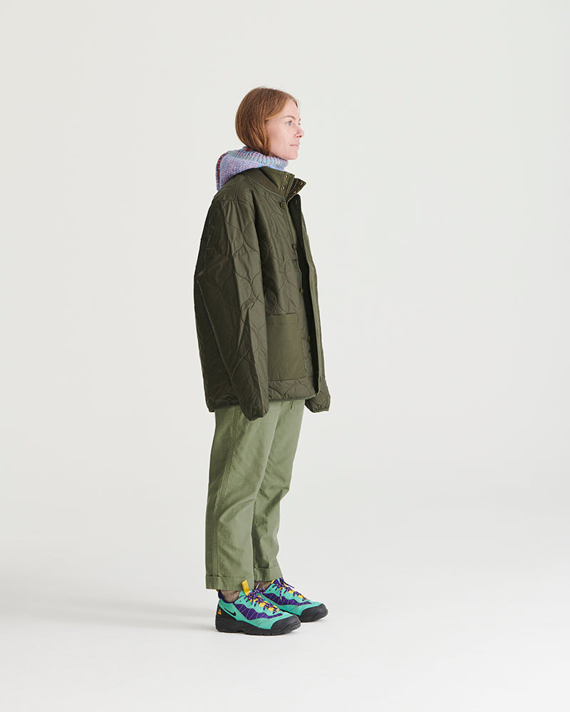 Forest Floor Bison Ultralight Liner Jacket (Side): Person wearing olive quilted jacket, matching pants, colorful sneakers, knit hood