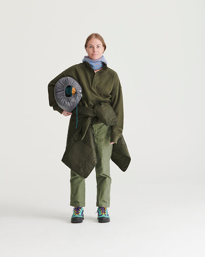 Forest Floor Bison Ultralight Liner Jacket (In-use): Woman wearing olive quilted liner jacket, holding packed sleeping bag, outdoors-ready outfit