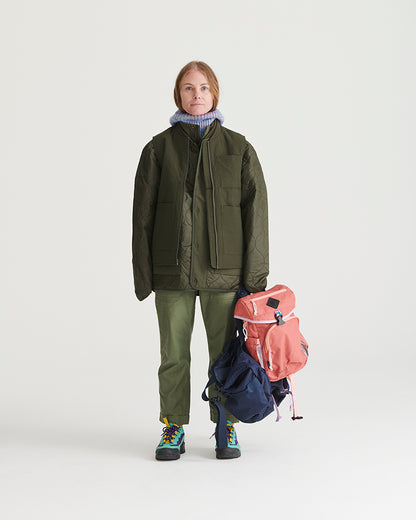 Forest Floor Bison Ultralight Liner Jacket (In-use): Woman in olive quilted jacket holding coral and navy backpacks