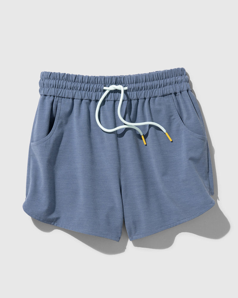 Stone Blue The Responsible Swim Short (Flat-lay): Slate blue drawstring shorts with white cord, yellow tips, side pockets