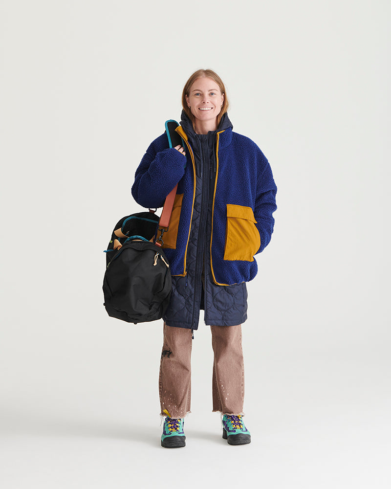 Night Sky Bison Ultralight Long Liner Jacket (In-use): Woman in navy quilted long jacket carrying black duffel bag, smiling