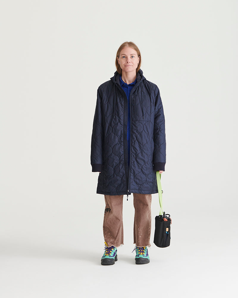 Night Sky Bison Ultralight Long Liner Jacket (In-use): Woman wearing navy quilted hooded long jacket, brown pants, colorful boots