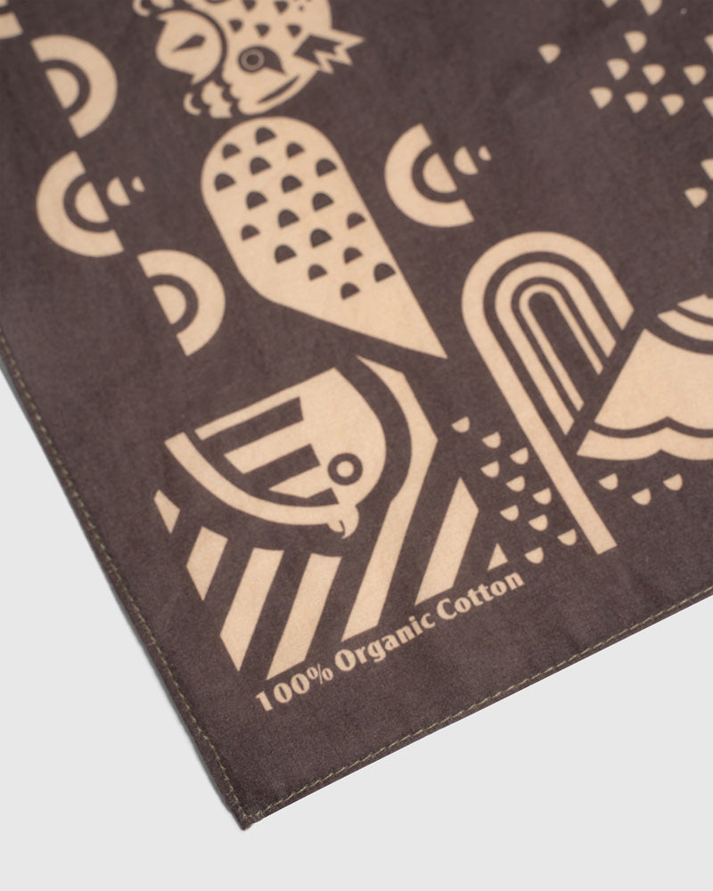 Dark Brown Organic Hoot Bandana (Detail): Dark brown bandana corner showing tan geometric bird print and organic cotton label