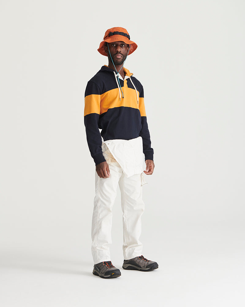 Tangerine Organic Bucket Stash Hat (In-use): Man wearing orange bucket hat with navy striped hoodie and white cargo pants