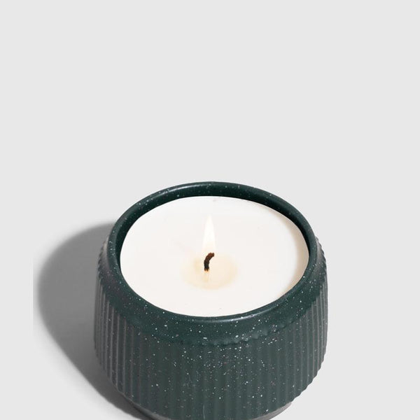 DARK GREEN 14 oz. Ceramic Keepsake Candle - Tioga Woods (Angle): Round dark teal ribbed ceramic vessel holding white wax with lit wick