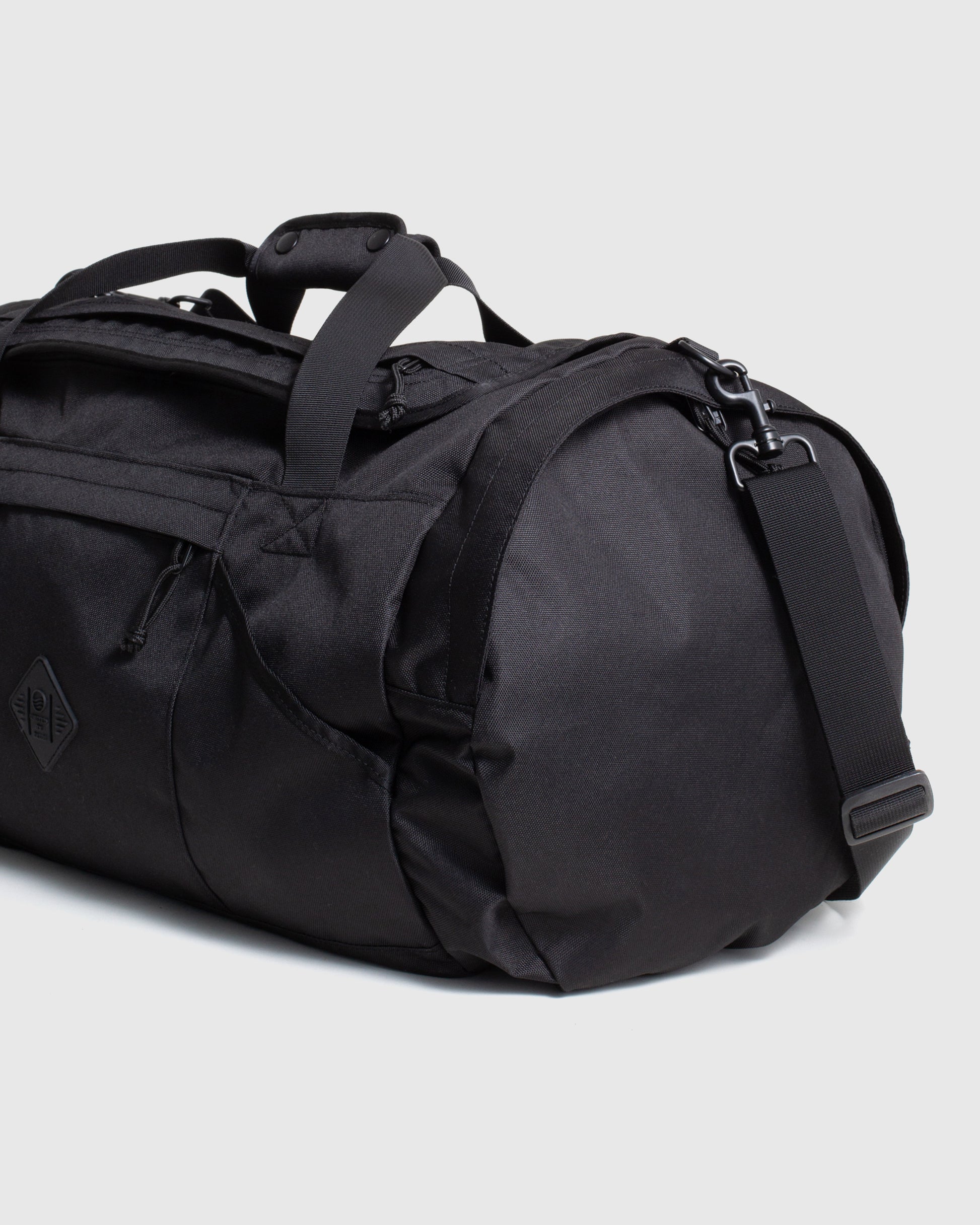 Black (R)evolution™ 55L Carry-On Duffle (Angle): Black duffle bag showing side panel, carry handles, and shoulder strap clip