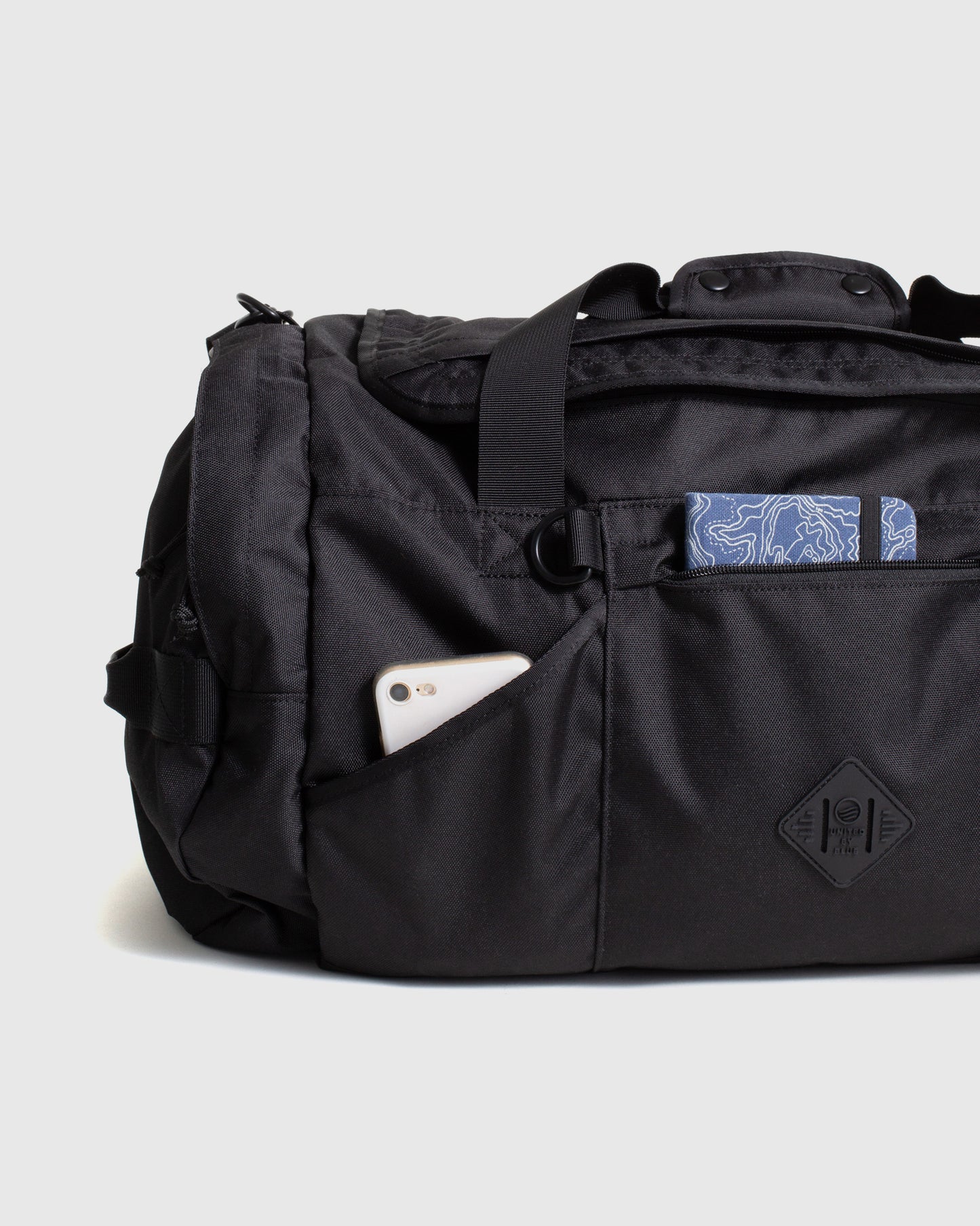 Black (R)evolution™ 55L Carry-On Duffle (Detail): Black duffle side pocket holds a phone; blue topographic wallet visible