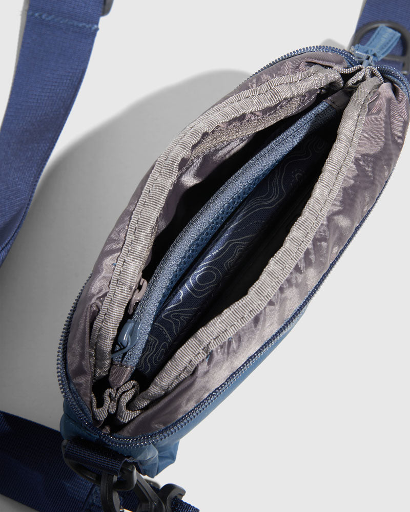Deep Sea (Re)active™ 2L Convertible Crossbody (Detail): Navy crossbody bag open, showing gray interior lining with inner zip pocket