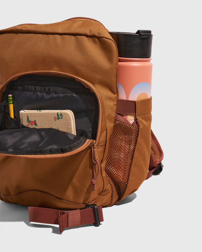 Camel (R)evolution™ 9L Sidekick (Detail): Open front pocket reveals pencil and notebook beside a coral water bottle