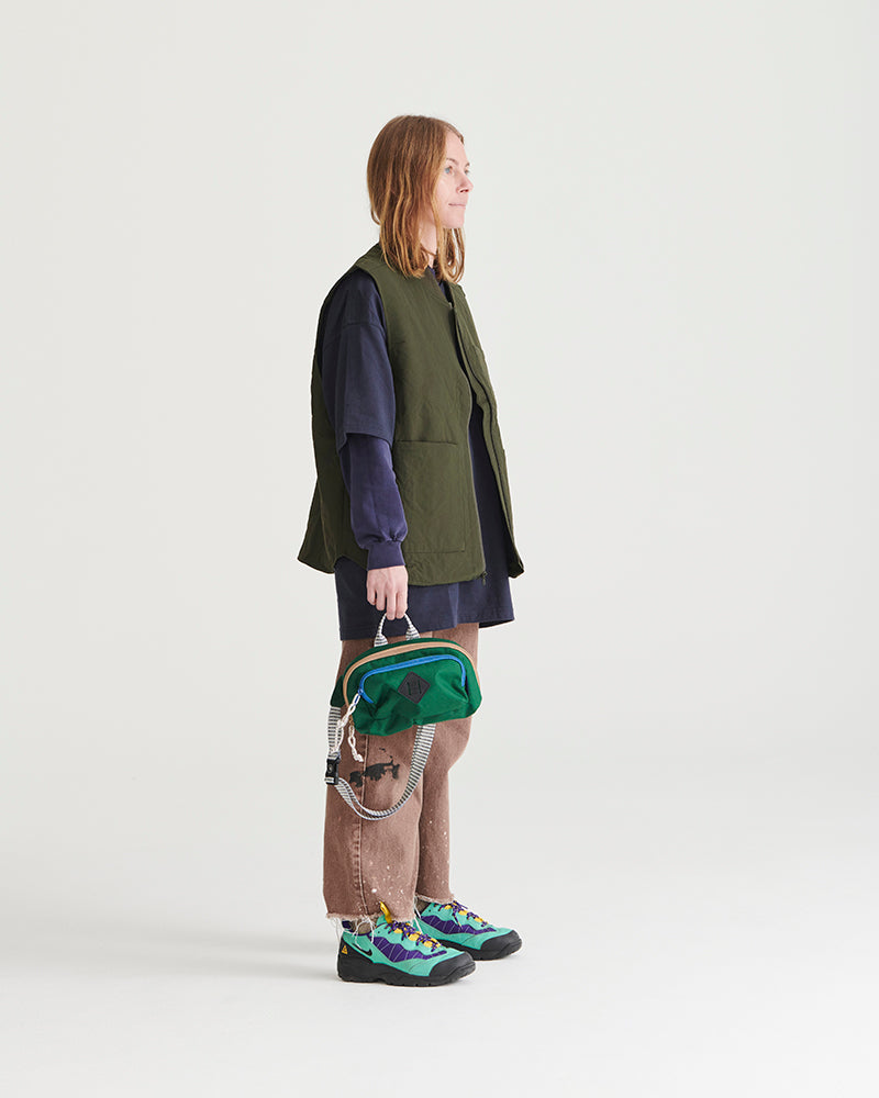 Pine (R)evolution™ 3L Utility Fanny Pack (In-use): Person holding green and blue small bag with rope handle, side view