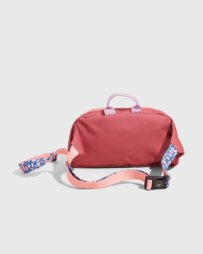 (R)evolution™ 3L Utility Fanny Pack (Angle): Red fanny pack with lavender handle, patterned blue and pink adjustable strap