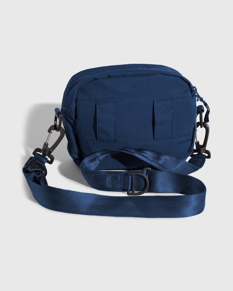 Blueberry (Re)active™ 2L Convertible Crossbody (Back): Navy blue crossbody bag, back view, MOLLE webbing, black carabiner clips, adjustable strap