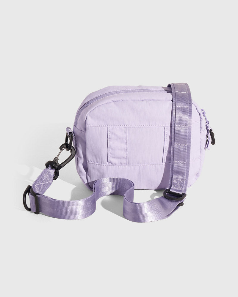 Lavender (Re)active™ 2L Convertible Crossbody (Angle): Light purple small crossbody bag with quilted panels and black hardware clips