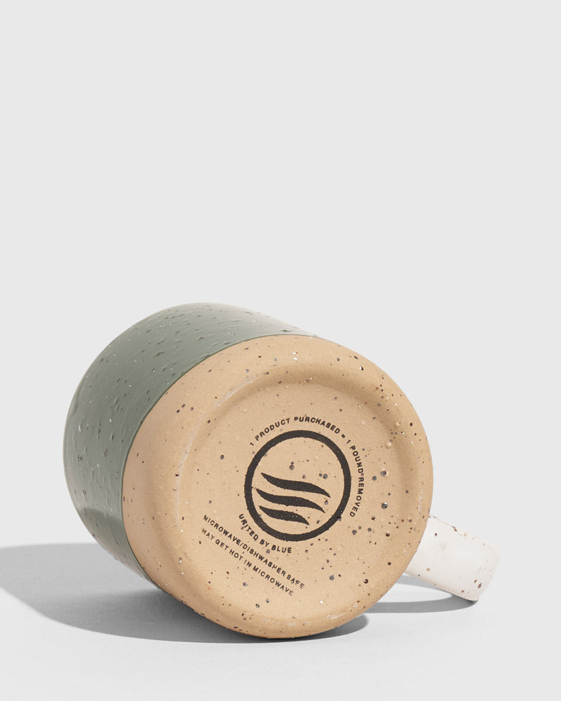 Pine 8 oz. Stoneware Mug (Detail): Bottom of sage green speckled mug showing brand logo and care icons