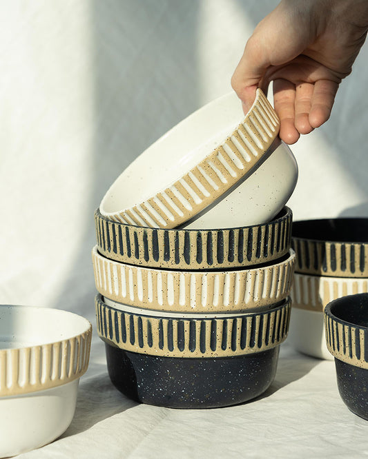 Eggshell Stoneware Stackable Bowl (In-use): Hand lifting ribbed cream bowl from stack of three patterned bowls