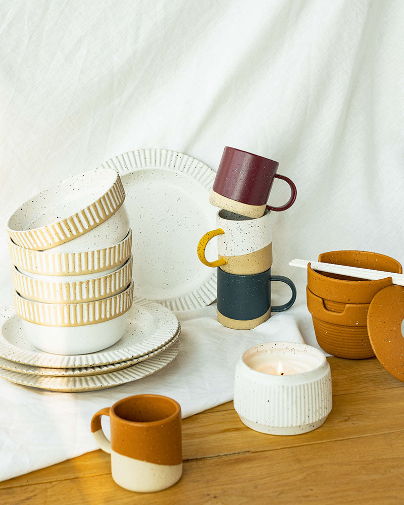 Eggshell Stoneware Stackable Bowl (Lifestyle): Stacked white speckled bowls with ribbed texture beside plates and mugs