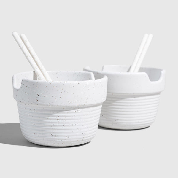 Eggshell Stoneware Stackable Noodle Bowl Set (Angle): Two speckled white ribbed bowls with chopstick rests and white chopsticks