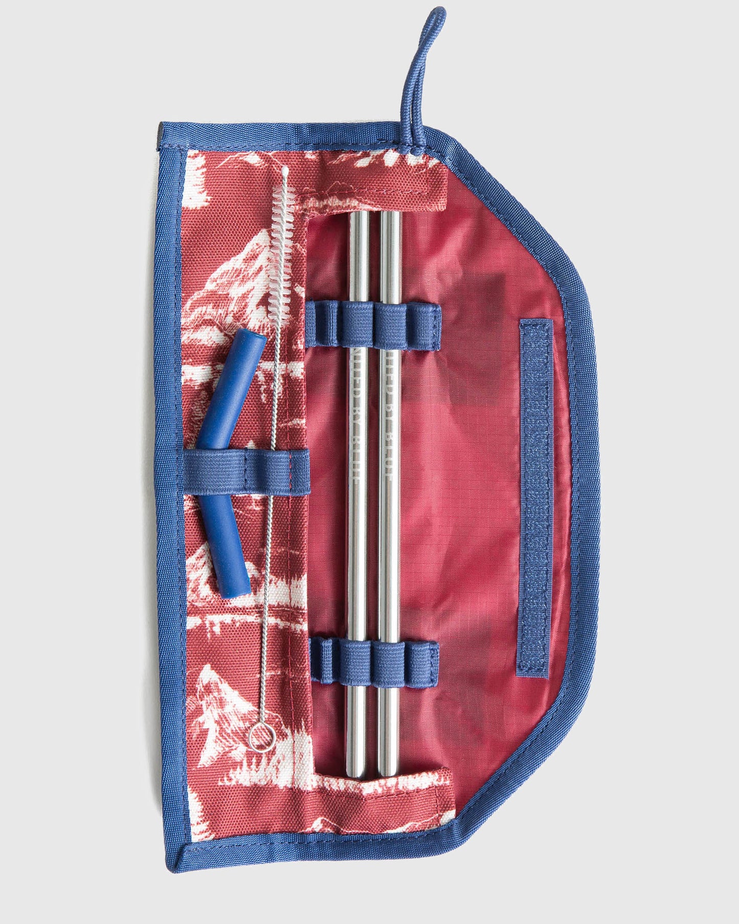 Sapphire The Straw Kit (Flat-lay): Open blue and red mountain-print case holding two metal straws and cleaning brush