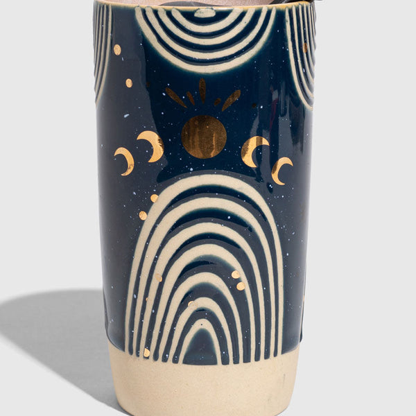 Nightfall Blue 10 oz. Insulated Stoneware Travel Mug (Angle): Navy ceramic tumbler with cream arches, gold sun, moons, and black lid