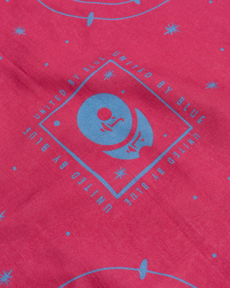 Beet Organic Bandana (Detail): Close-up of blue diamond logo and star pattern on pink fabric