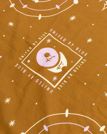 Smoky Ochre Organic Bandana (Detail): Mustard fabric with celestial print, crescent moon logo, and brand text