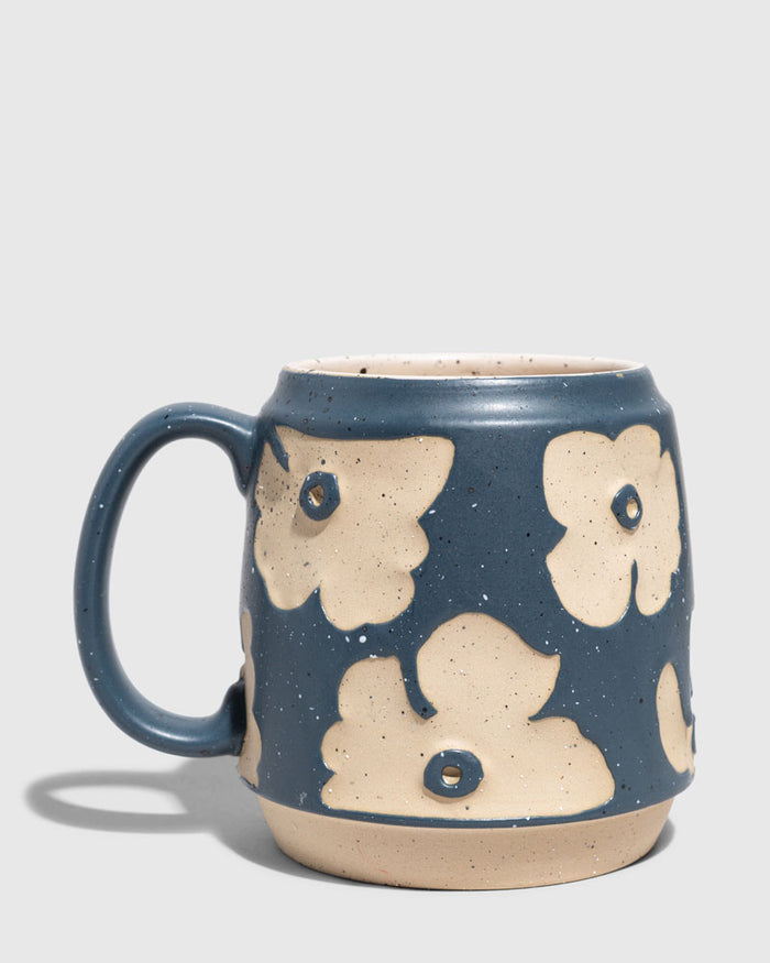Eclipse Blue 16 oz. Stoneware Mug (Angle): Barrel-shaped mug with raised cream floral shapes on matte blue speckled glaze