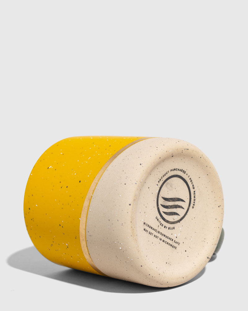 Butterscotch 8 oz. Stoneware Mug (Detail): Yellow speckled mug shown upside-down, revealing unglazed ceramic base with logo