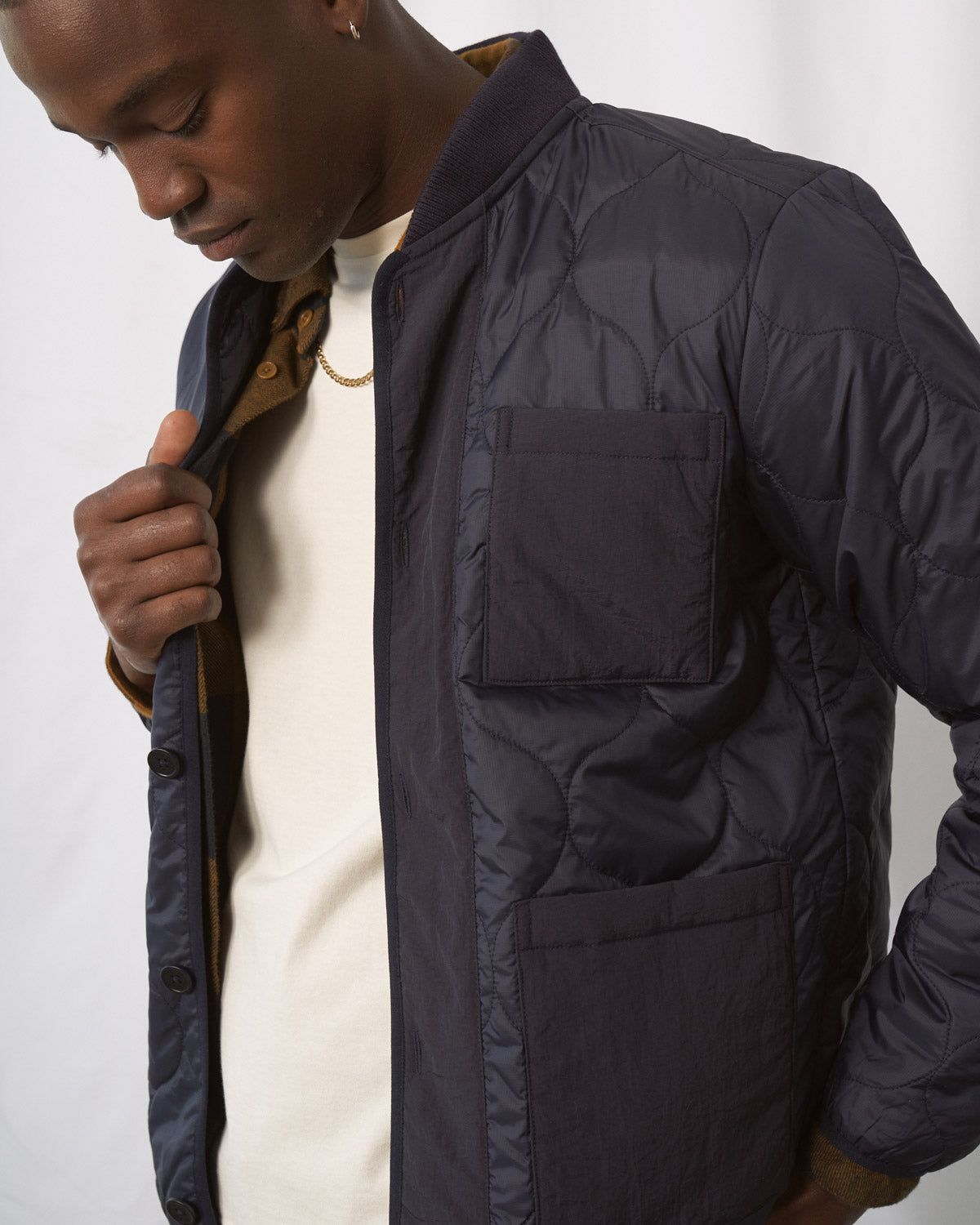 Night Sky Bison Ultralight Liner Jacket (Detail): Man holding open dark navy quilted bomber jacket, chest patch pocket visible