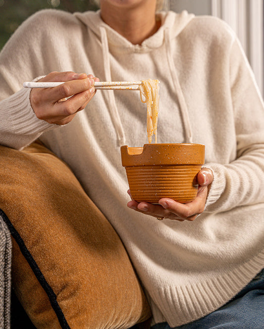 Caramel Stoneware Stackable Noodle Bowl Set (In-use): Person in cream hoodie eating noodles from speckled terracotta-style bowl with chopsticks
