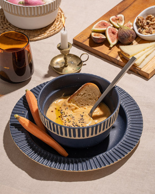 Slate Stoneware Stackable Plate (Lifestyle): Dark blue ridged plate and bowl with soup, figs, and carrots nearby