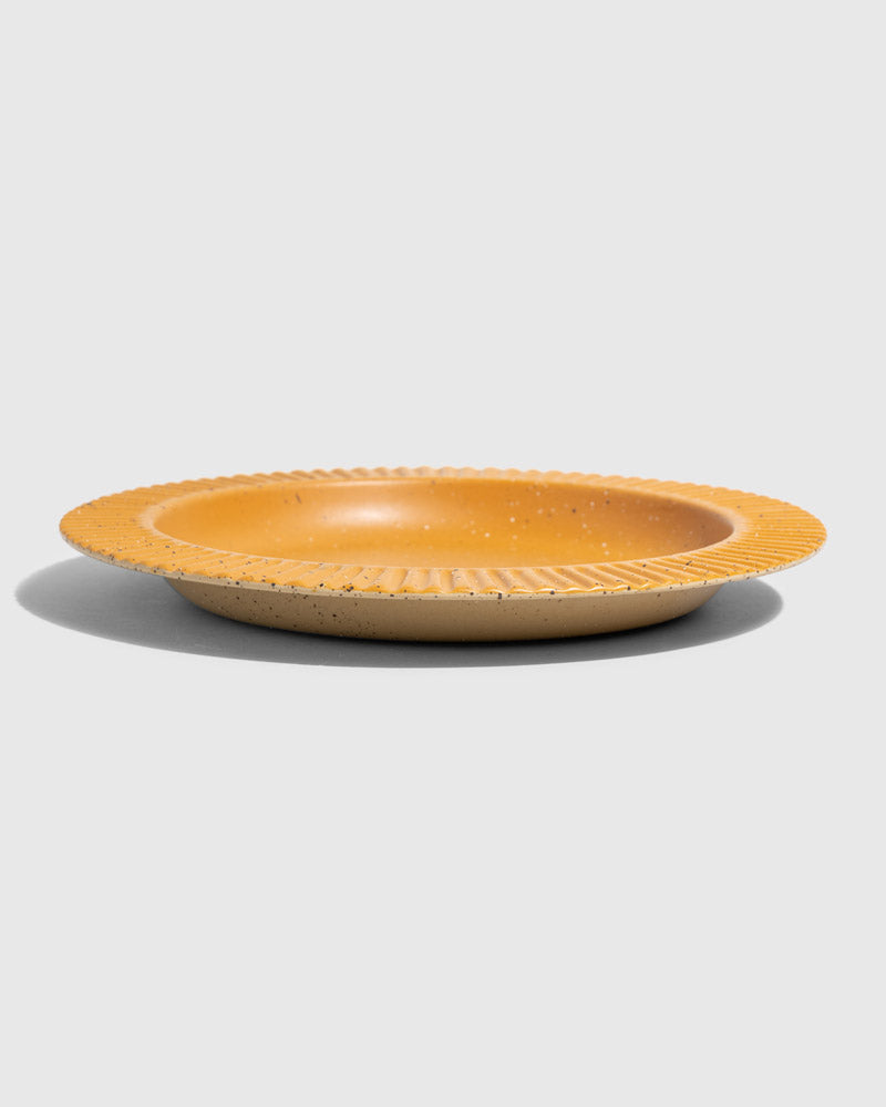 Caramel Stoneware Stackable Plate (Angle): Round golden-yellow ceramic plate with ribbed textured rim and speckled finish