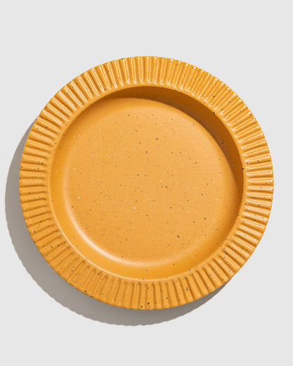 Caramel Stoneware Stackable Plate (Flat-lay): Round mustard-yellow speckled ceramic plate with ridged fluted rim border