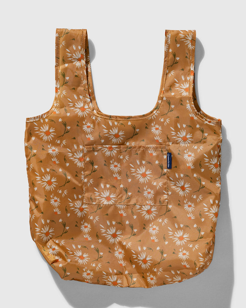 The Packable Tote (Flat-lay): Golden-tan tote with white daisy print, dual straps, and front pocket