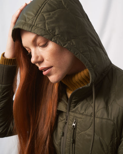 Forest Floor Bison Ultralight Long Liner Jacket (In-use): Woman with red hair wearing olive quilted hooded jacket, eyes closed