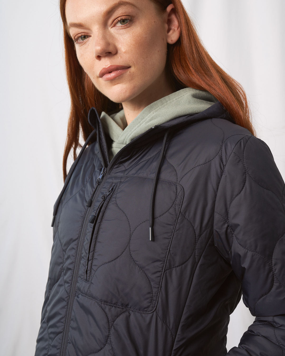 Night Sky Bison Ultralight Long Liner Jacket (Angle): Dark navy quilted zip-up jacket with circular stitch pattern, worn by woman