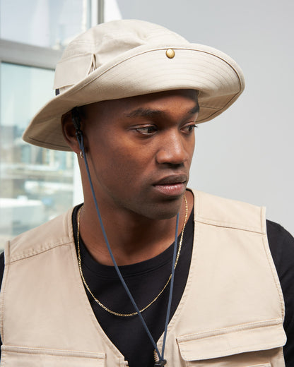 Bone Organic Bucket Stash Hat (In-use): Man wearing tan wide-brim hat with gold button and chin cord