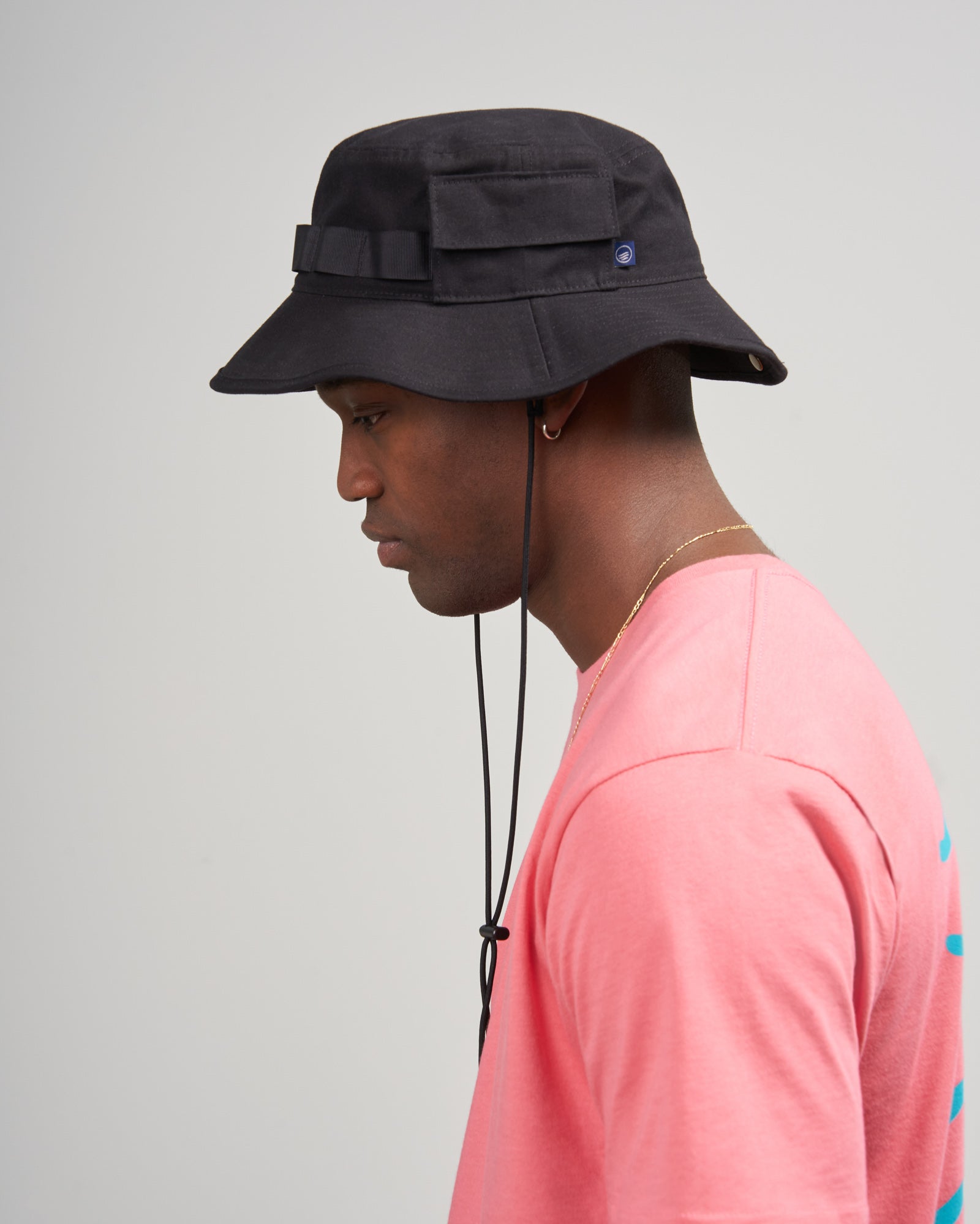 Obsidian Organic Bucket Stash Hat (Side): Black bucket hat with chin cord worn by male model, pink shirt