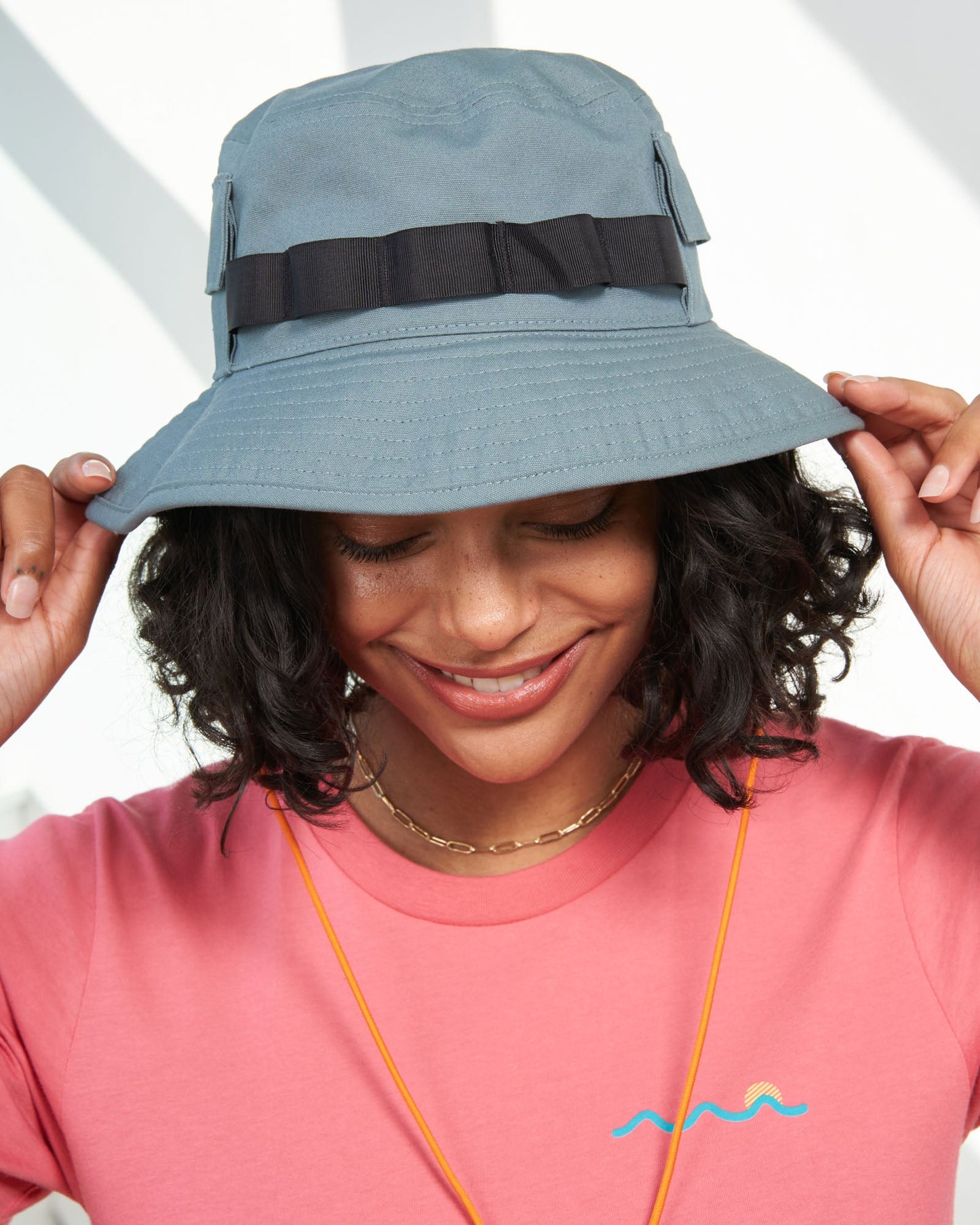 Sky Blue Organic Bucket Stash Hat (In-use): Smiling woman wearing slate blue wide-brim bucket hat with dark ribbon band