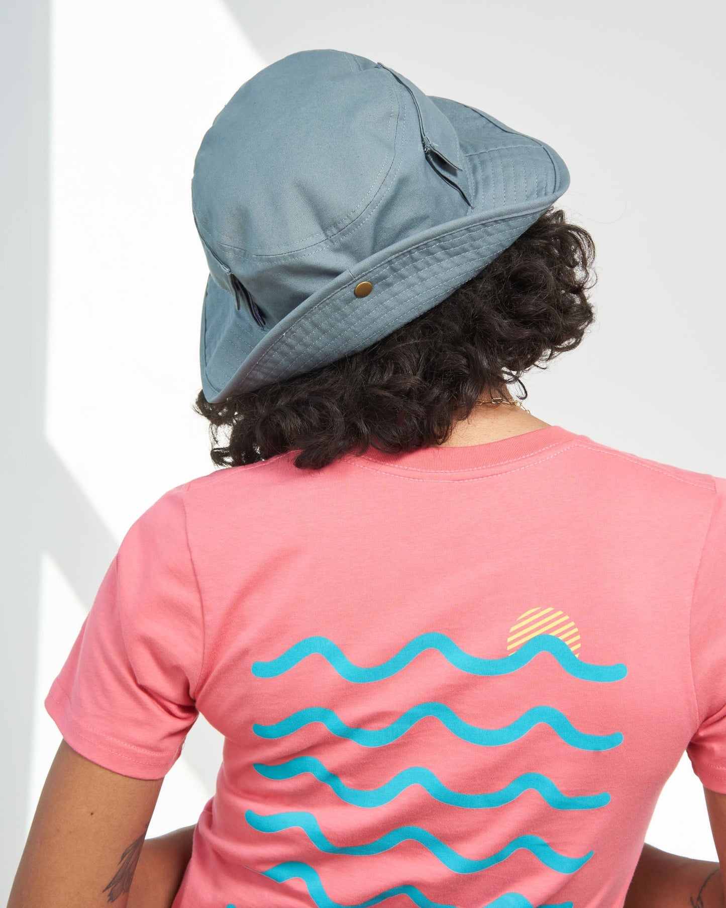 Sky Blue Organic Bucket Stash Hat (In-use): Person seen from behind wearing dusty blue wide-brim hat with snap closures