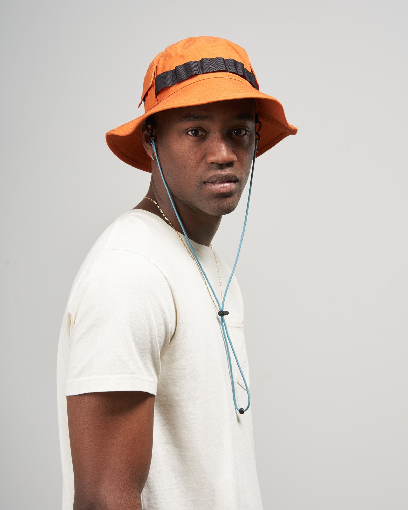 Tangerine Organic Bucket Stash Hat (In-use): Man wearing orange bucket hat with dark band and teal chin cord
