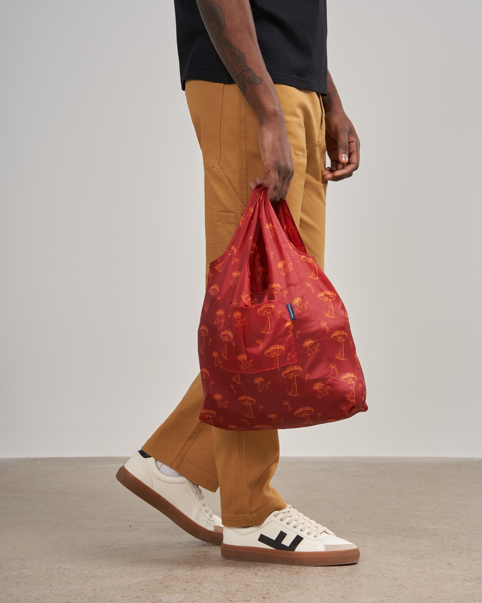 The Packable Tote (In-use): Red reusable tote with orange mushroom print held by walking person