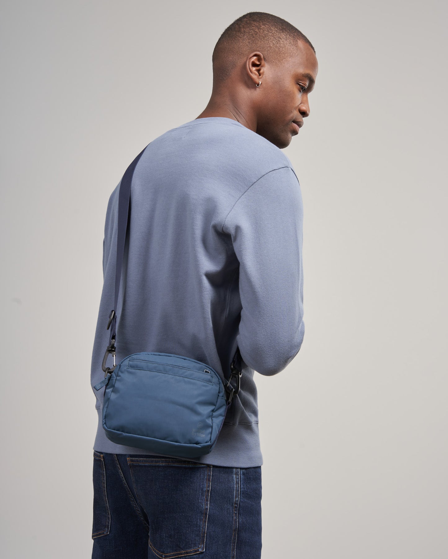 Deep Sea (Re)active™ 2L Convertible Crossbody (In-use): Man wearing teal crossbody bag over blue sweatshirt and jeans