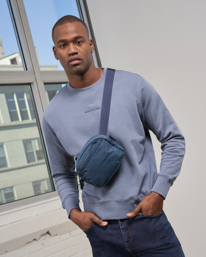 Deep Sea (Re)active™ 2L Convertible Crossbody (In-use): Man wearing teal crossbody sling bag over grey crewneck sweatshirt indoors