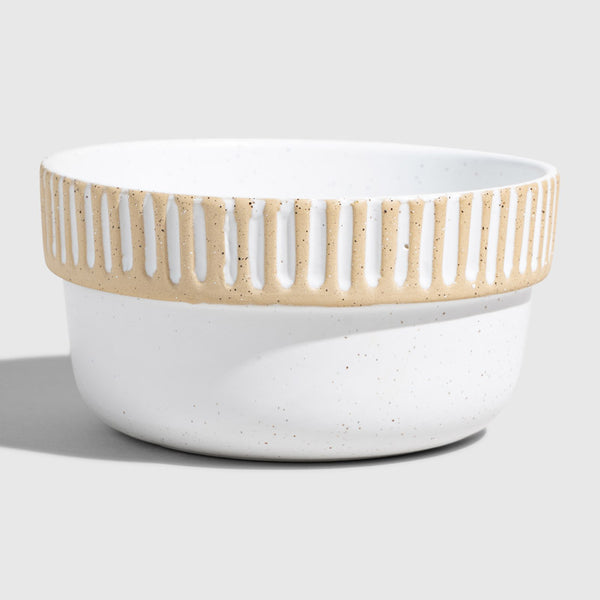 Eggshell Stoneware Stackable Bowl (Angle): Round white speckled bowl with tan carved vertical stripe band near rim