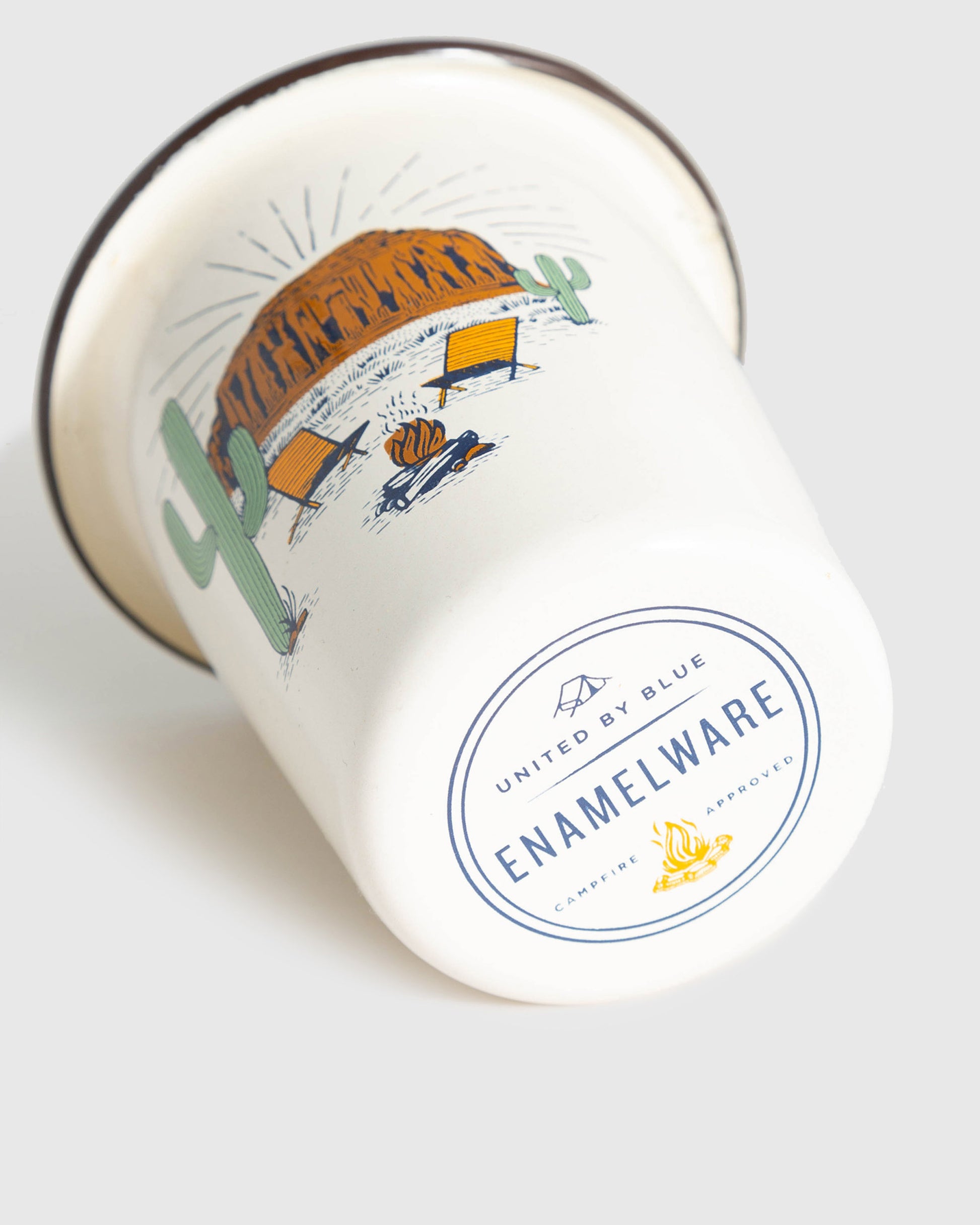 Cream Desert Chill Enamel 12 Oz. Tumbler (Angle): White enamel tumbler tipped on side, desert campfire scene, brand stamp visible