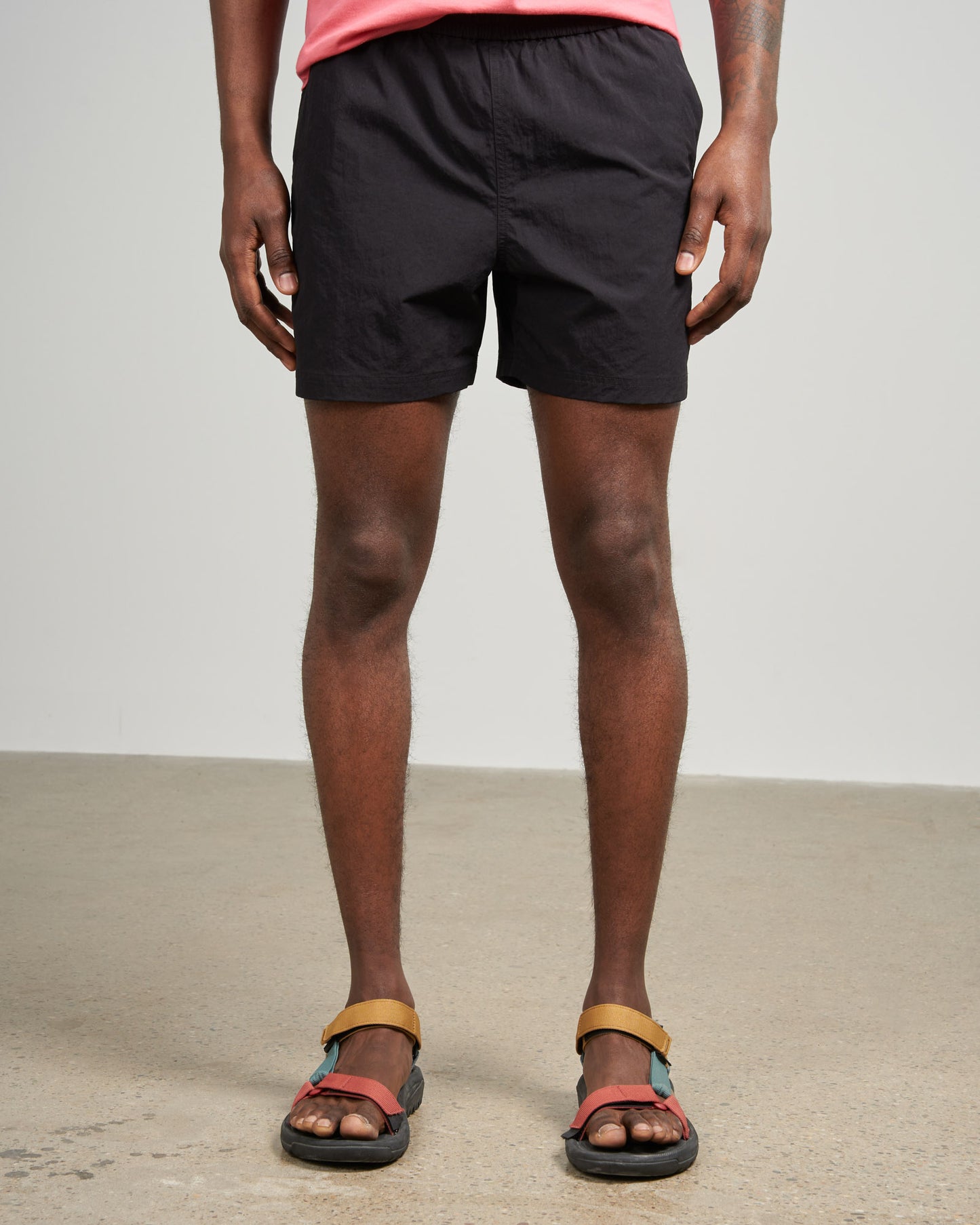 Black Recycled Sport Short (Front): Black elastic-waist shorts on male model with colorful sport sandals