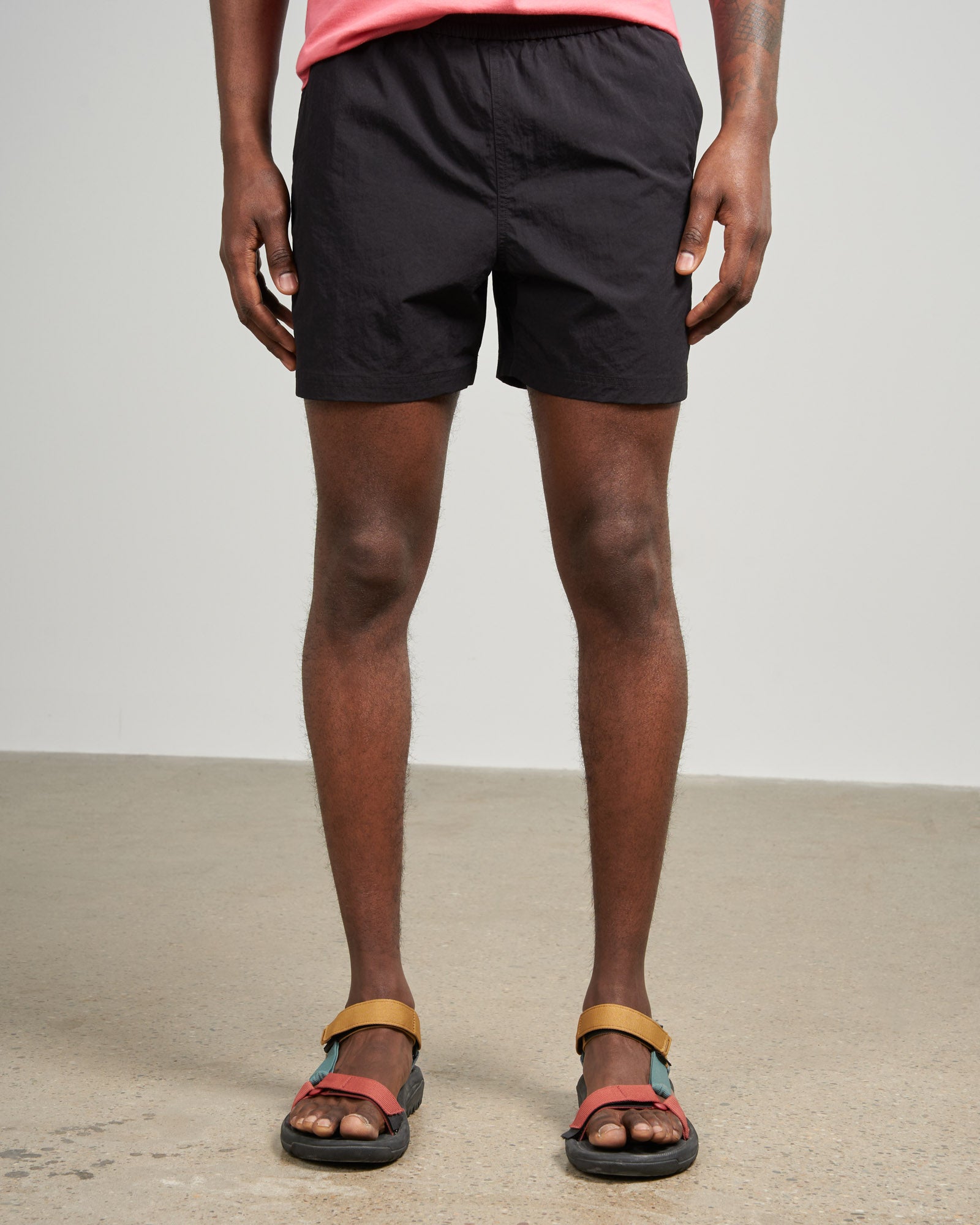 Black Recycled Sport Short (Front): Black elastic-waist shorts on male model with colorful sport sandals